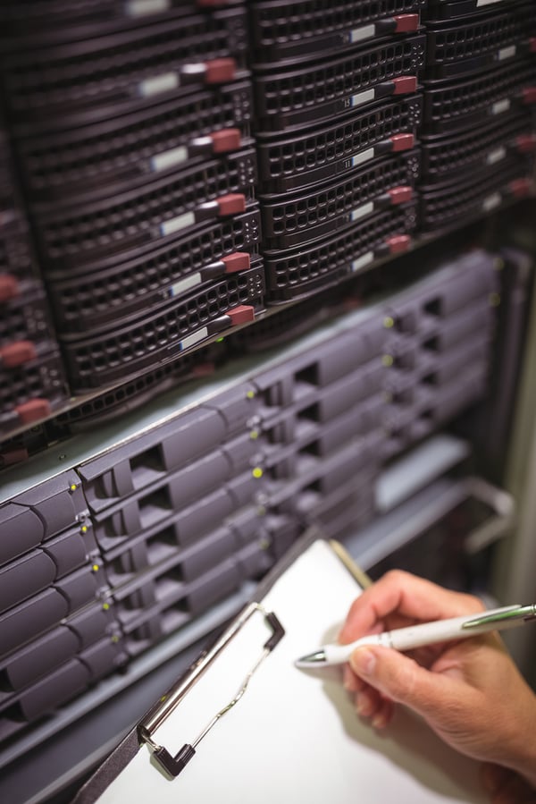 Close-up of technician maintaining record of rack mounted server on clipboard in server room